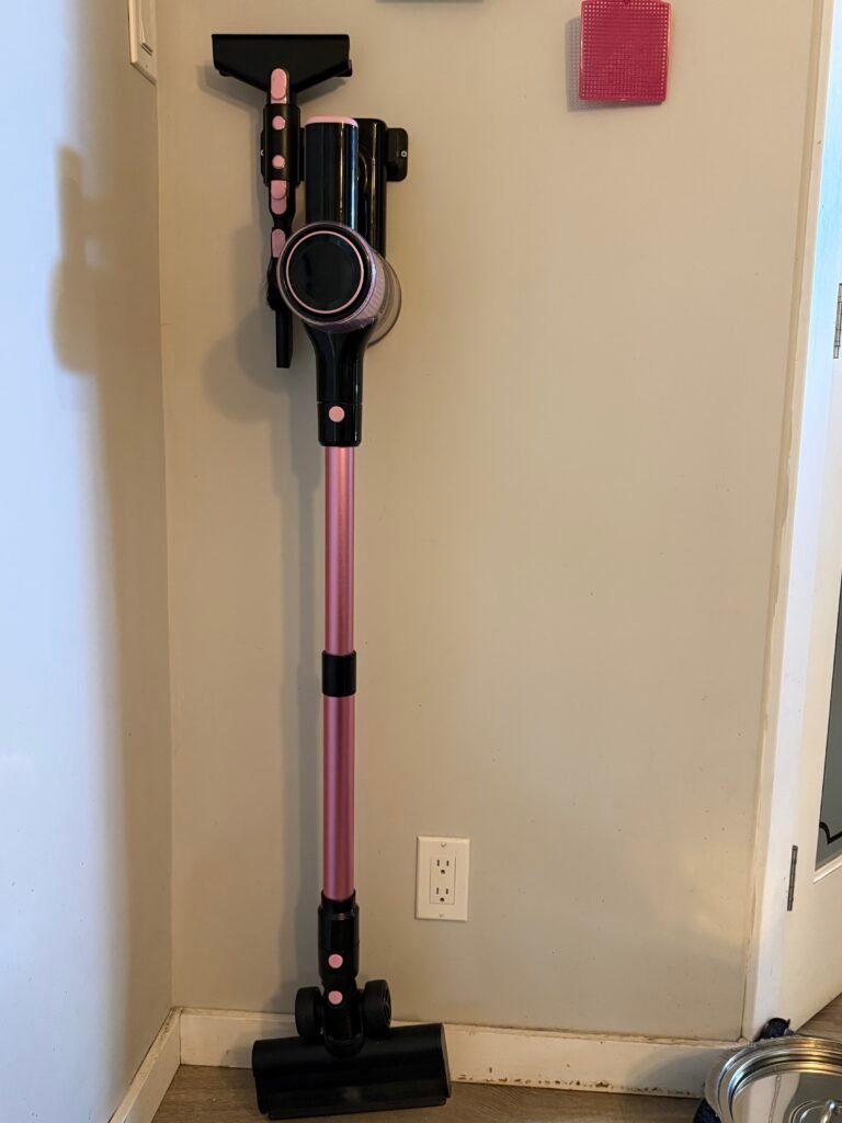 Pink Cordless vacuum cleaner hanging upright on wall mount holder.